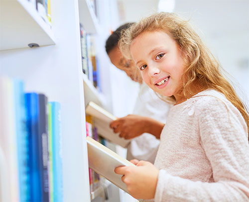 Young child looking through books on a library shelf